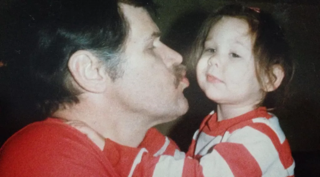 A man embraces his young daughter in his arms and leans in for a kiss.