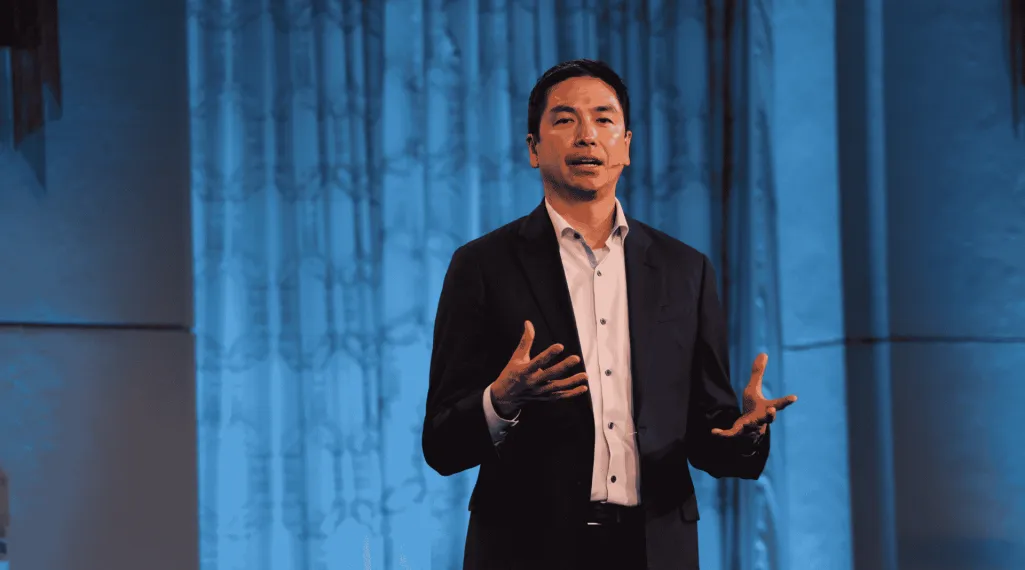 Dr. Christopher Lieu speaks onstage at the Colorectal Cancer Alliance Cure Summit, gesturing with both hands against a blue-lit backdrop.