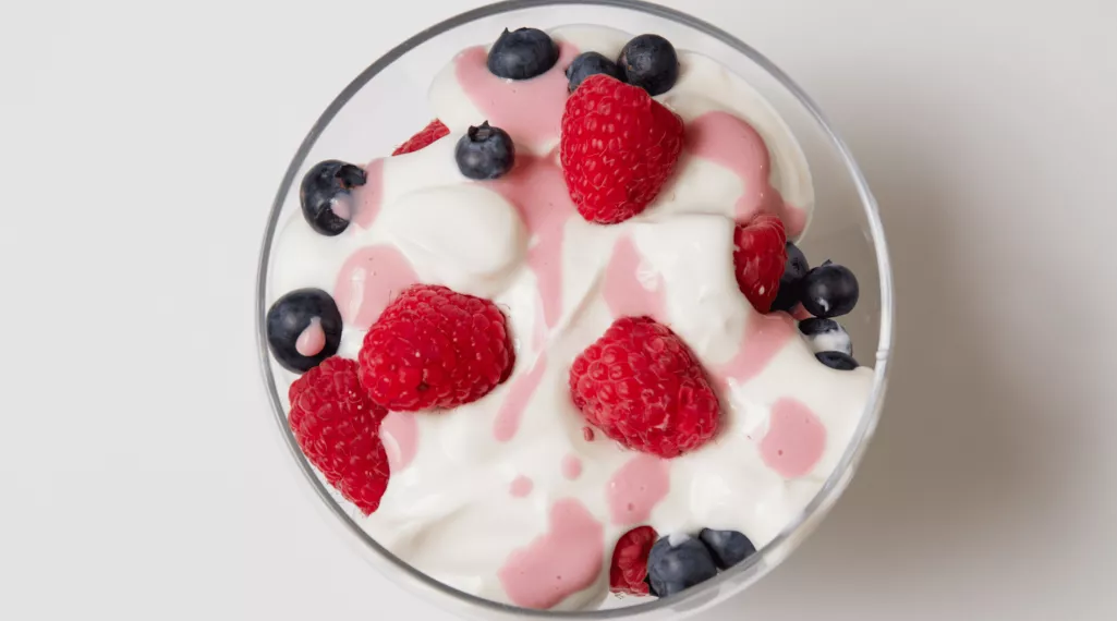 A bowl of plain yogurt with strawberries and blueberries.