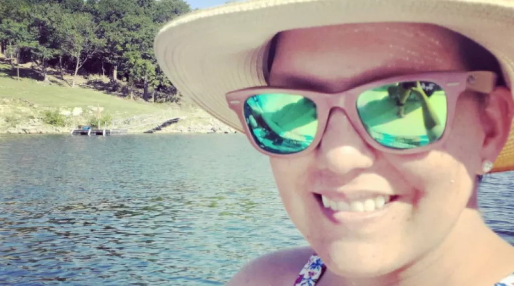 Yvonne at a lake, wearing reflective sunglasses and a hat.