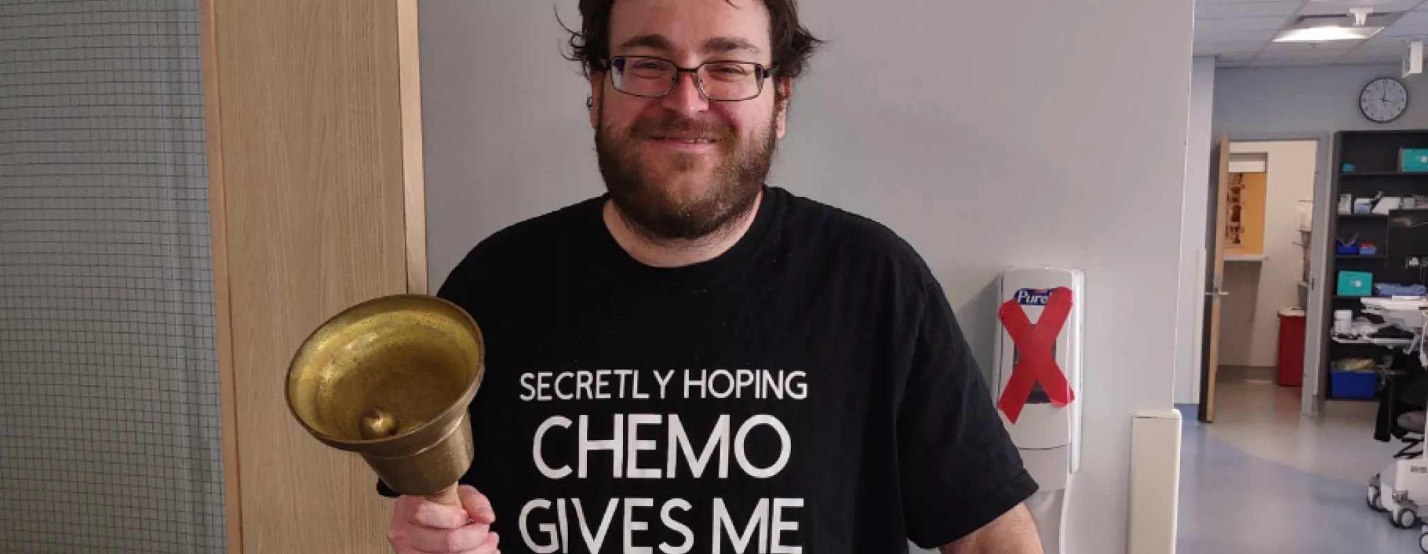 Man wearing "Secretly hoping chemo gives me superpowers" shirt holding a big bell