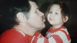 A man embraces his young daughter in his arms and leans in for a kiss.
