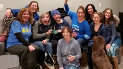 Un defensor del cáncer colorrectal está rodeado de amigos, familiares y dos perros en un sofá, pasando un momento divertido juntos.