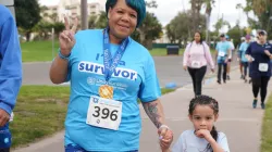 Black woman (survivor T-shirt) walking with small child