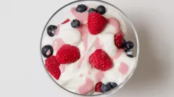 A bowl of plain yogurt with strawberries and blueberries.