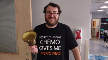 Gabriel Leblanc rings a bell while wearing a shirt that says, "Secretly hoping chemo gives me superpowers."