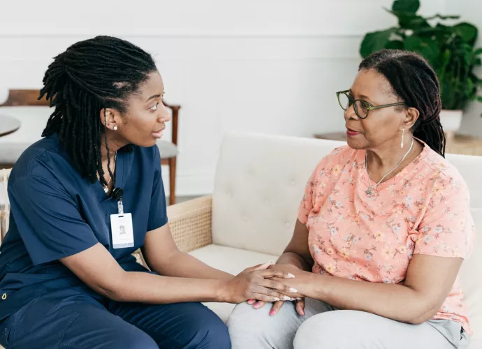 Two Black women, one a nurse and one a patient, discuss treatment.