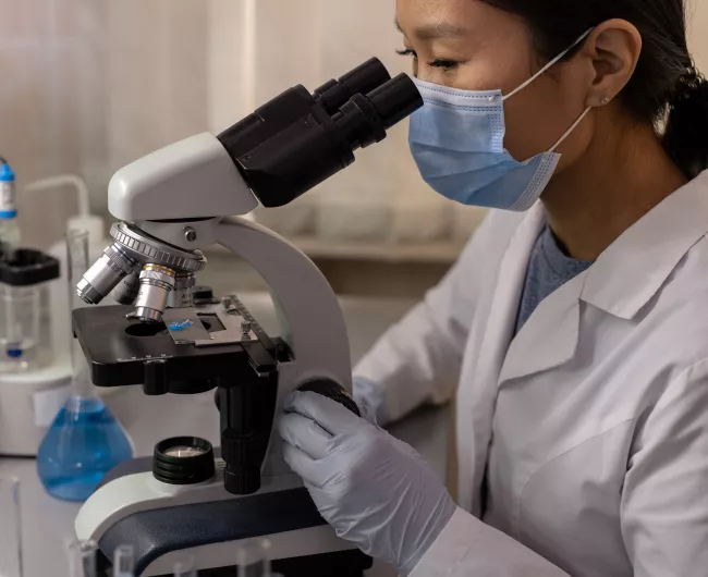 female scientist with vials using a microscope