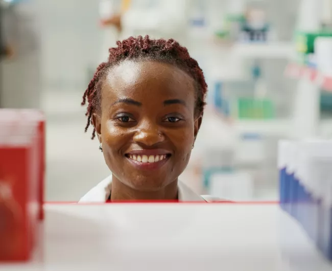 black pharmacist smiling behind medicine shelf