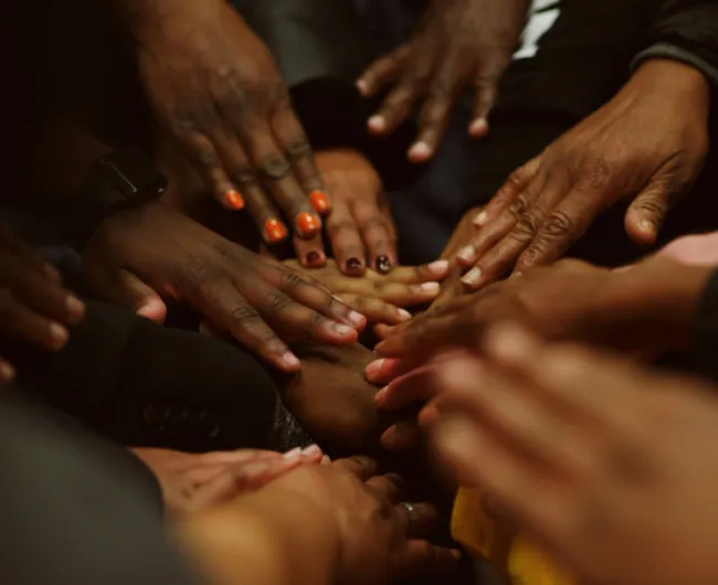 A group of hands stacked together in the center, symbolizing unity, teamwork, and support.
