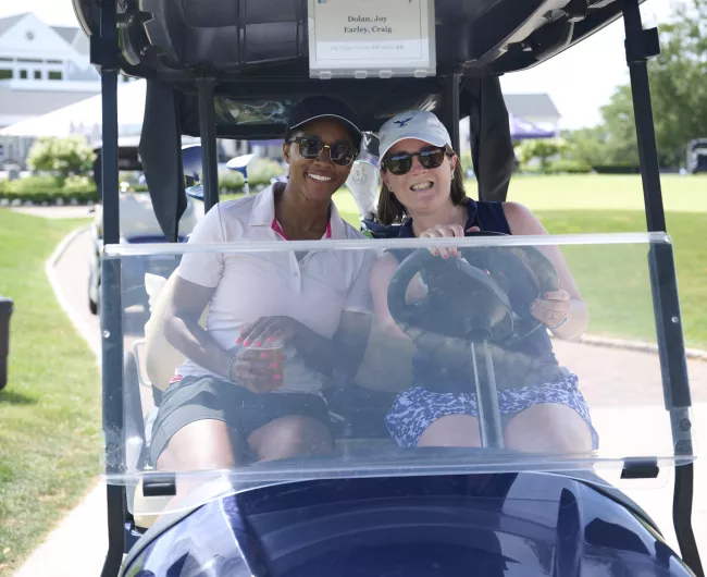 two women smiling sitting in a golf cart
