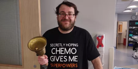 Man wearing "Secretly hoping chemo gives me superpowers" shirt holding a big bell